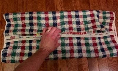 Hand holding plaid fabric over books to make cat scratch board.